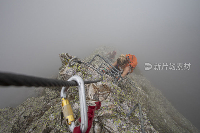 在雾中，一名年轻女子爬上via ferrata